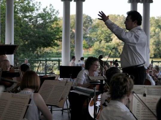 Inside the Como pavilion with Kenwood Orchestra performing on stage and the conductor with his arm raised.